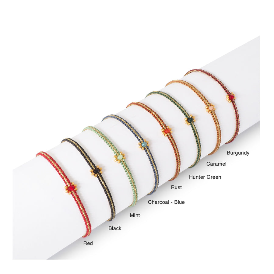 Stack of colorful Handmade Dainty Daisy Macrame Bracelets made with Italian waxed cord on a white surface. Colors: Burgundy, Caramel, Hunter Green, Rust, Charcoal Blue, Mint, Black, and Red.