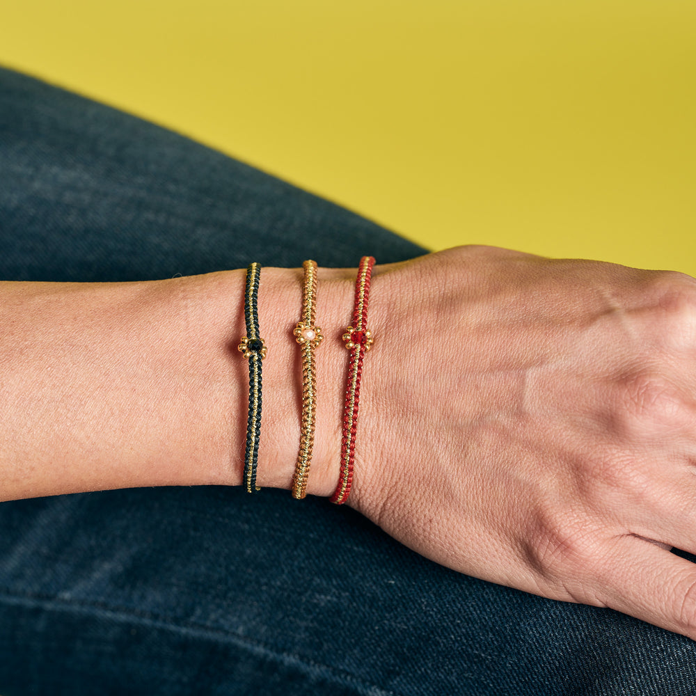 Three Macramé Dainty Daisy Bracelets with Czech Murano glass beads on a wrist against a yellow and blue background. Colors: Black, Caramel, and Red.