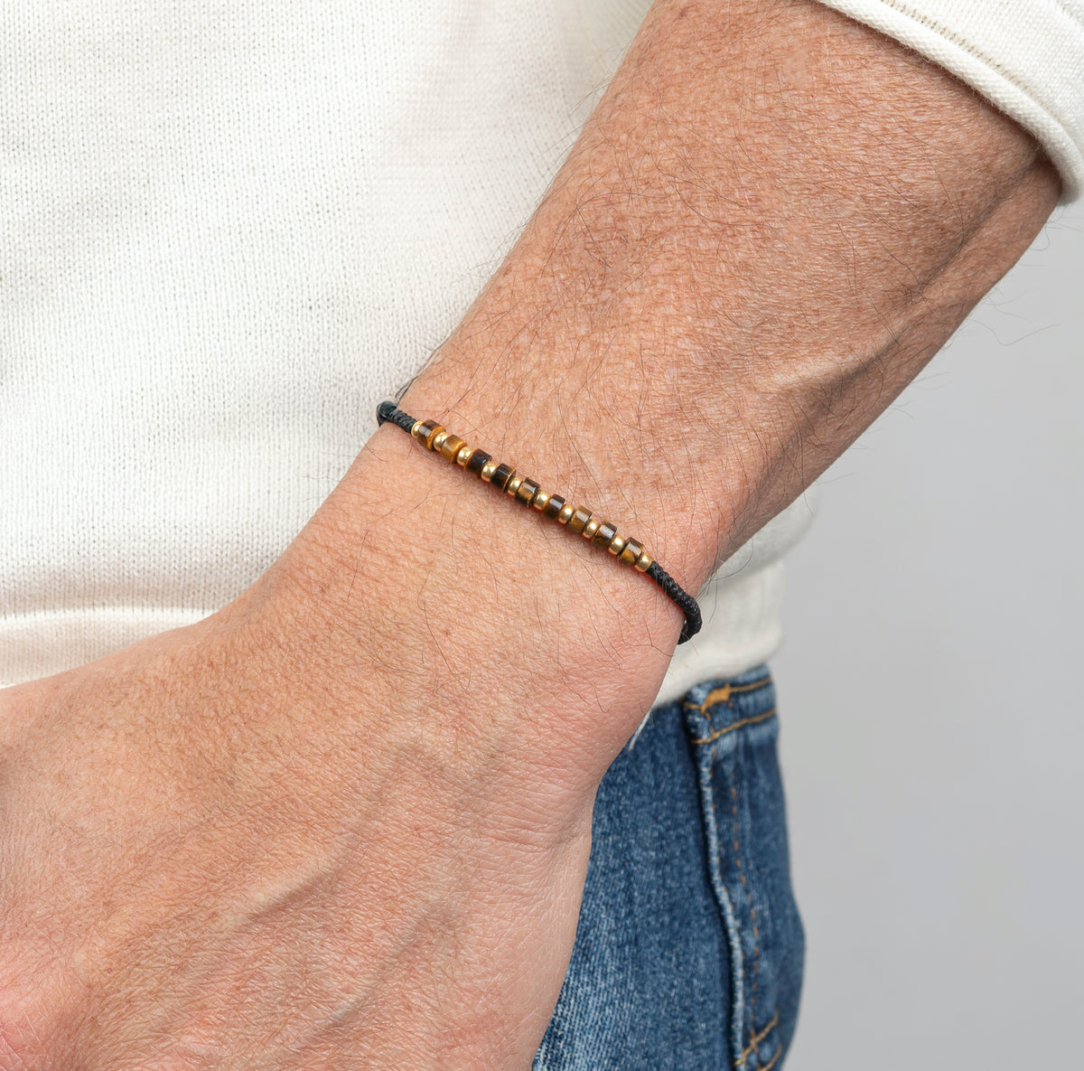 Man wearing men’s tiger eye and gold Miyuki bead bracelet on black wax cord, minimalist adjustable bracelet.