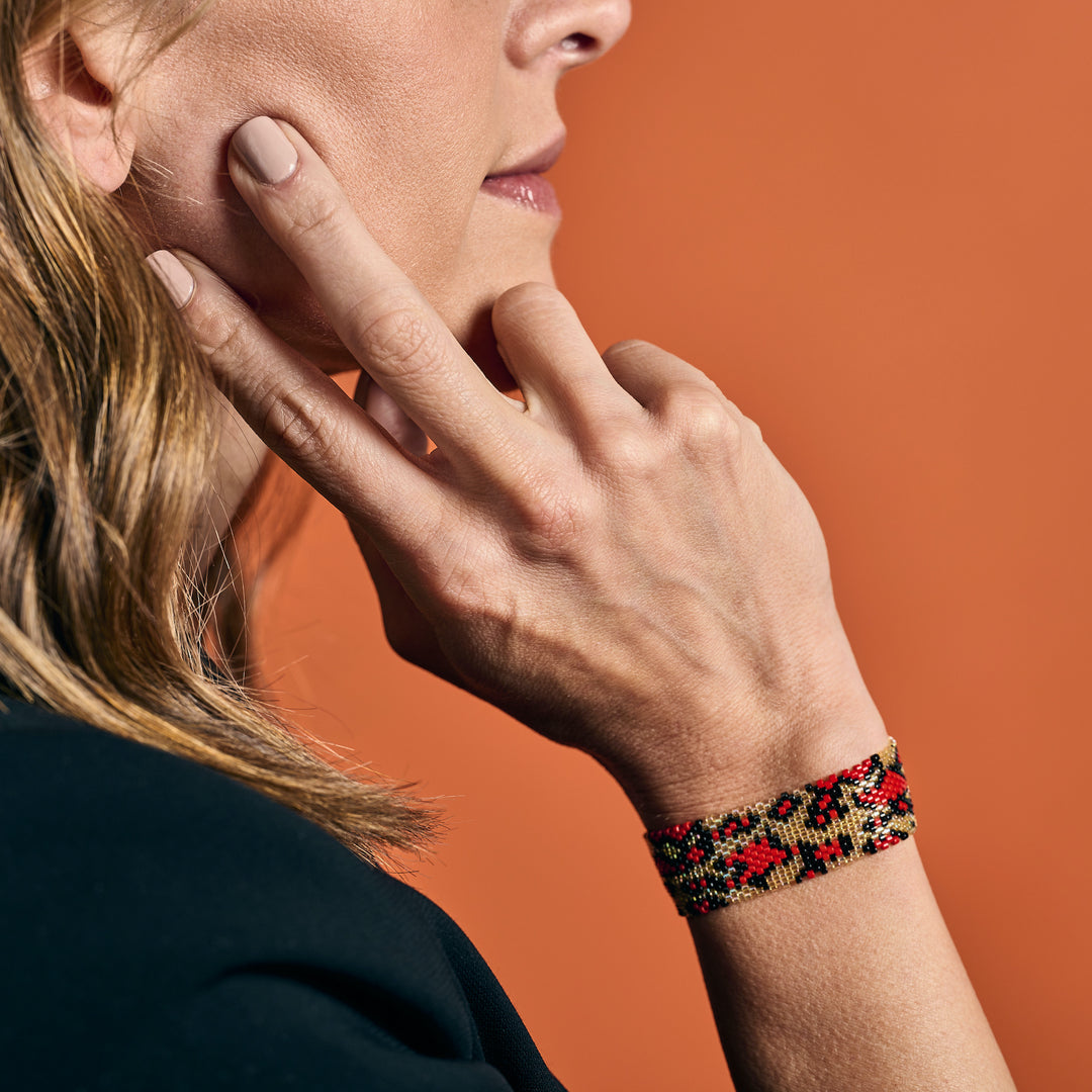 Handmade Leopard Miyuki beaded bracelet, red, black, and gold on a woman's wrist.
Colombian artisan jewelry, boho chic accessory.