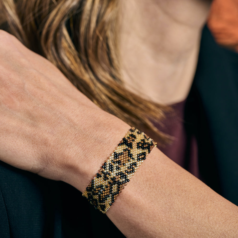 Handmade Leopard Miyuki beaded bracelet, brown, black, and gold on a woman's wrist.
Colombian artisan jewelry, boho chic accessory.
